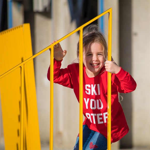 Blonde girl with red shirt with 'Ski you later' print by KMLeon behind yellow gate.