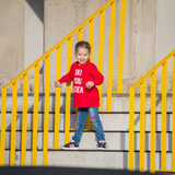 Blonde girl with red shirt with 'Ski you later' print by KMLeon next to yellow gate.