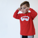 Young boy making glasses sign on face with fingers, wearing red shirt with long sleeves, with ski goggles print by KMLeon.