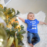 Little boy laying on white carpet, wearing blue shirt with 'Waiting for snow' print by KMLeon.