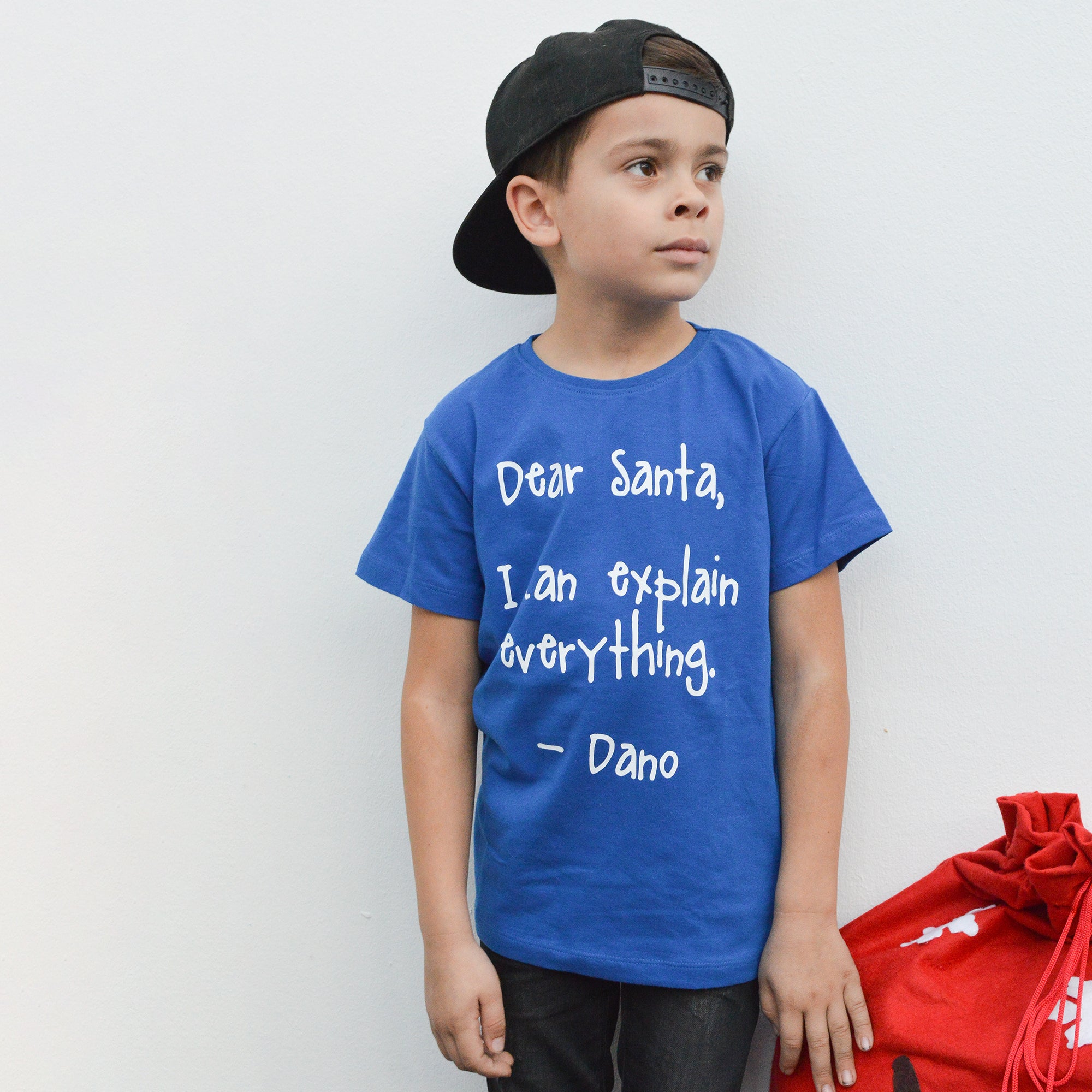 Boy with black cap and blue shirt with 'Santa, I can explain everything' shirt by KMLeon, looking guilty.