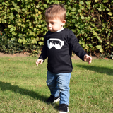 Little boy wearing black shirt with longs sleeves withh ski goggles print by KMLeon walking in park.