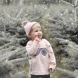 Blonde girl with pink beanie wearing pink shirt with long sleeves with glitter snow flake glasses print by KMLeon, looking at snow.