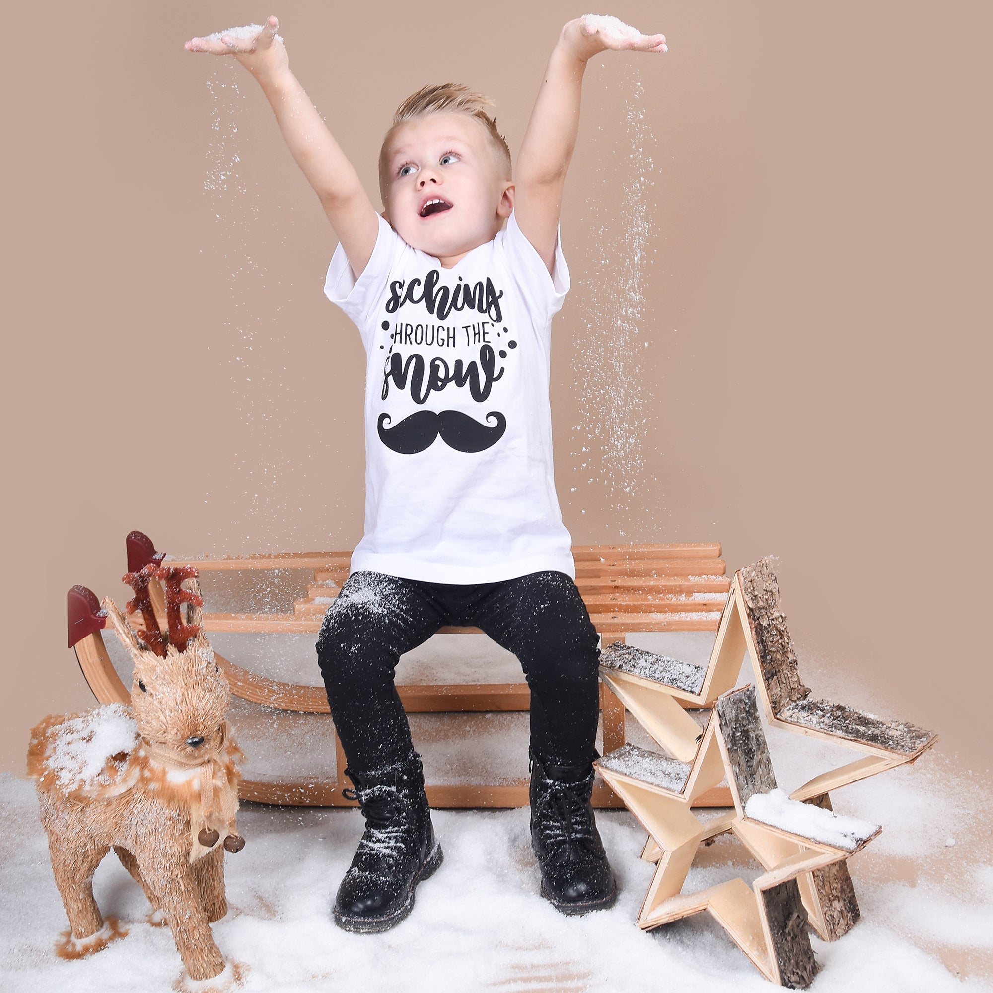 Blonde boy playing with snow, wearing white shirt with 'Staching through the snow' print by KMLeon.