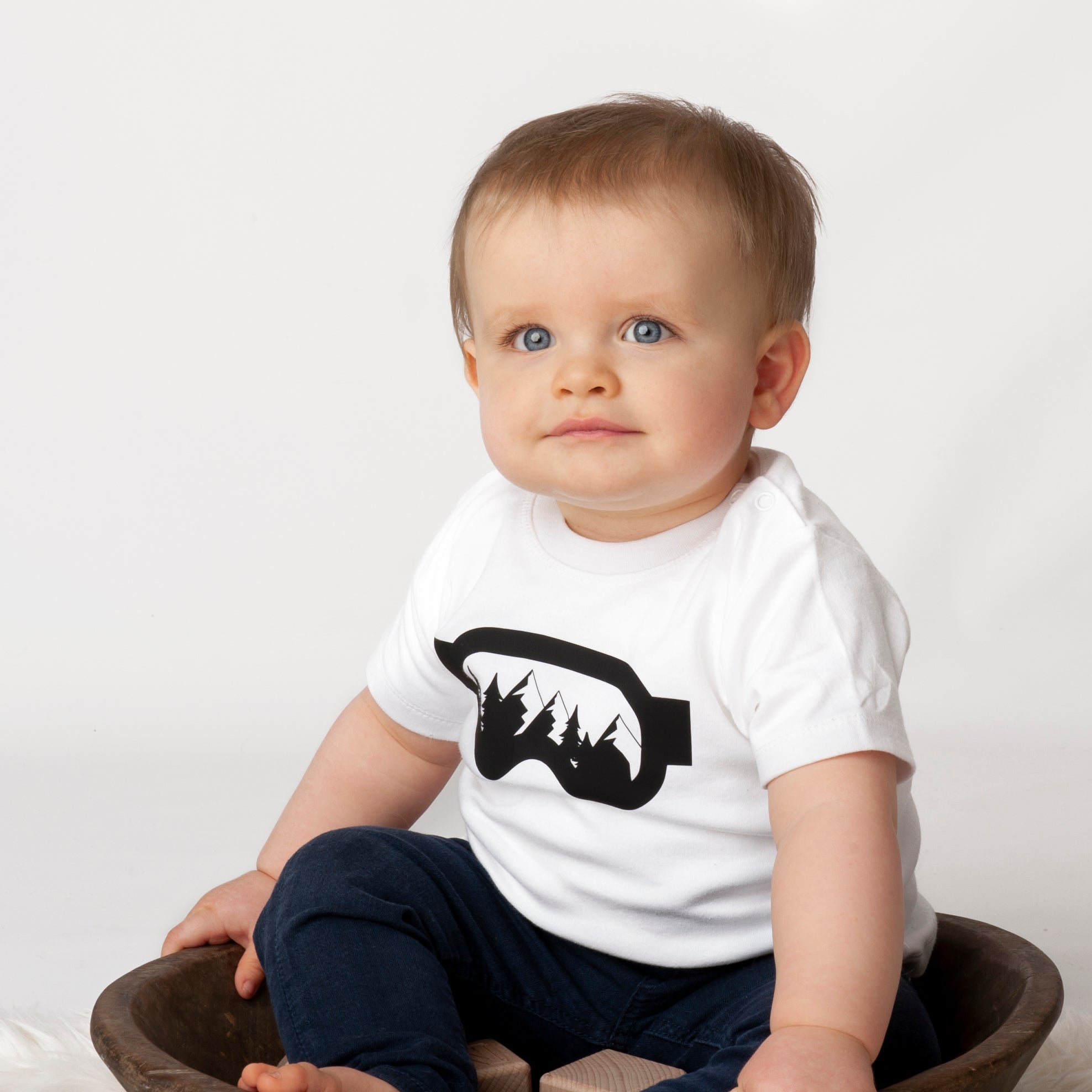 Little boy wearing white shirt with ski goggles print by KMLeon sitting in brown dish.