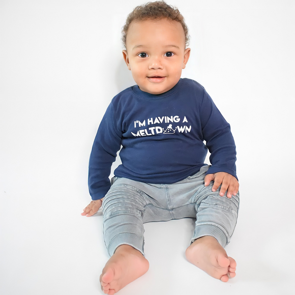 Smiling black boy sitting wearing navy shirt with longs sleeves with 'I'm having a meltdown' print by KMLeon.