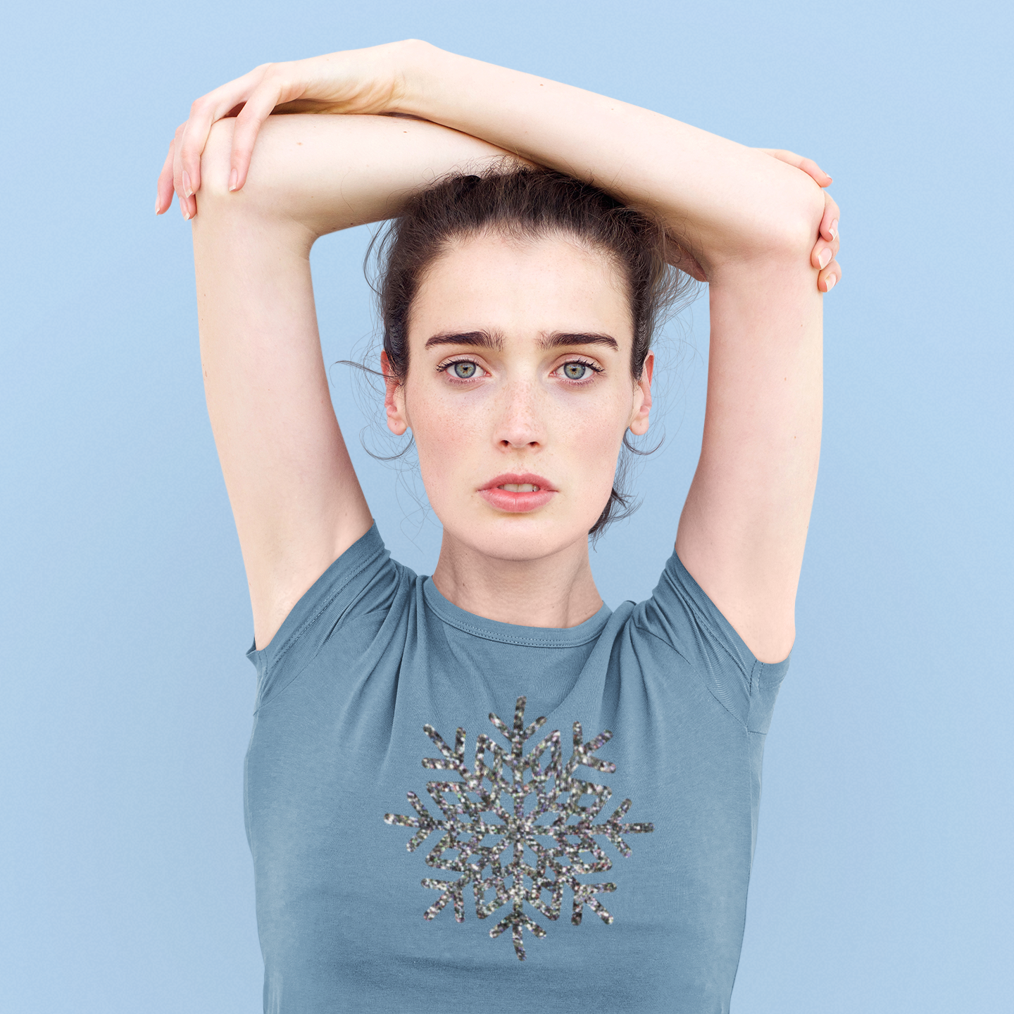 Woman wearing indigo shirt, with glitter snow star print by KMLeon, holding arms above head.